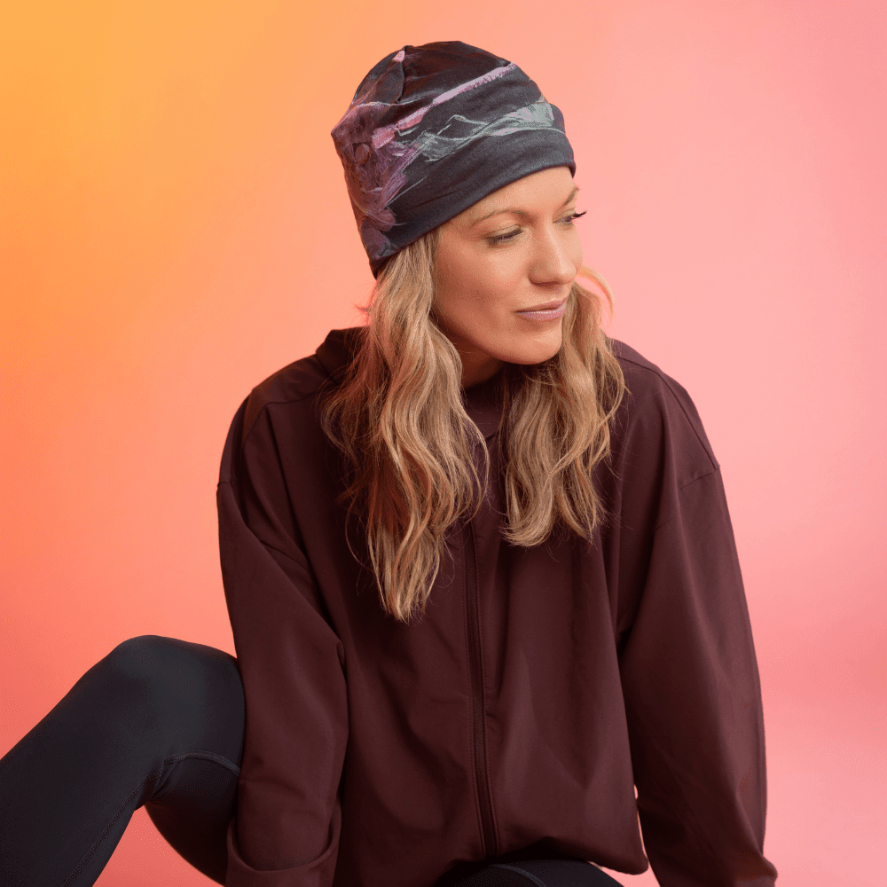 A woman wearing a black beanie with a pink and green floral art print looks thoughtfully to the side.