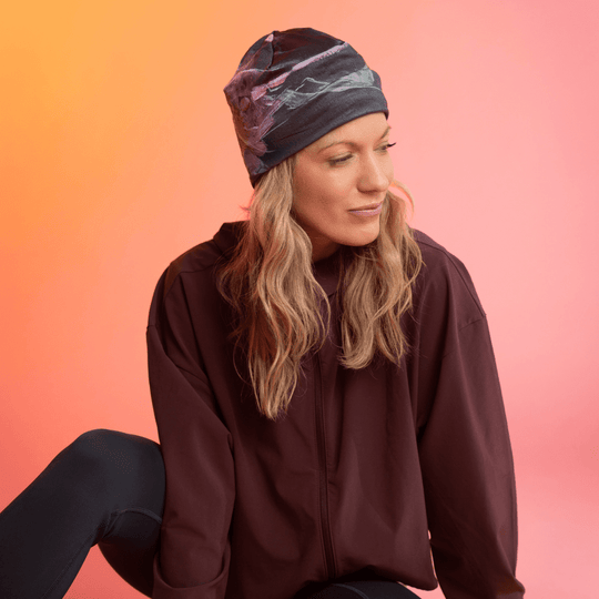 A woman wearing a black beanie with a pink and green floral art print looks thoughtfully to the side.