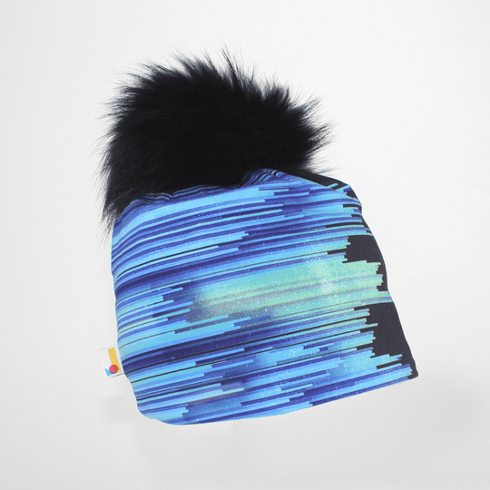 Tuque "Black War" à rayures abstraites bleues et violettes et gros pompon noir, sur fond blanc.