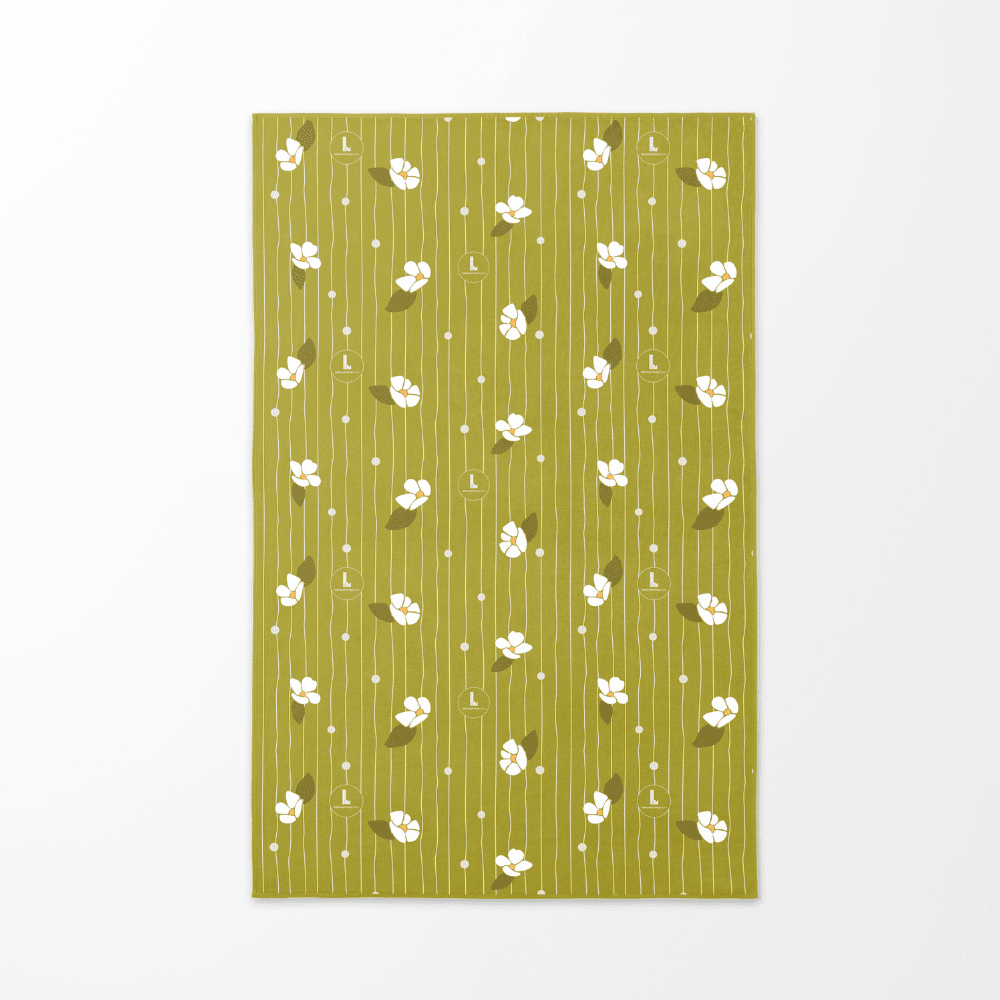 Le revers de la serviette de plage artistique Chrysalide, avec un fond vert doux et des motifs floraux blancs et des lignes verticales.