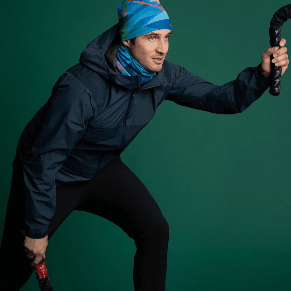 Homme portant une veste sombre et le tube de cou au motif abstrait ainsi qu'une tuque assortie, tenant des cordes d'entraînement.