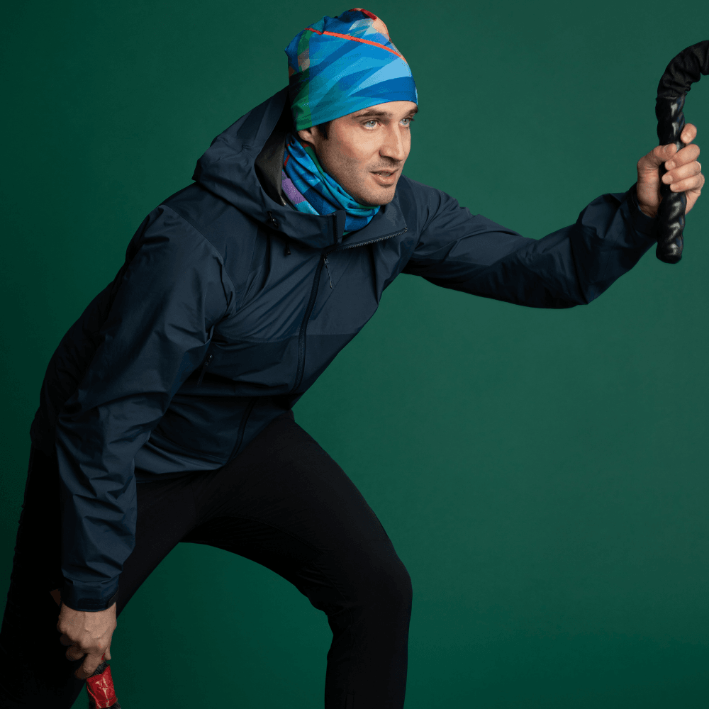 Homme portant une veste bleue et un cache-cou ainsi qu'une tuque assortis 'Motifs Géométriques Vifs', tenant une corde de fitness.