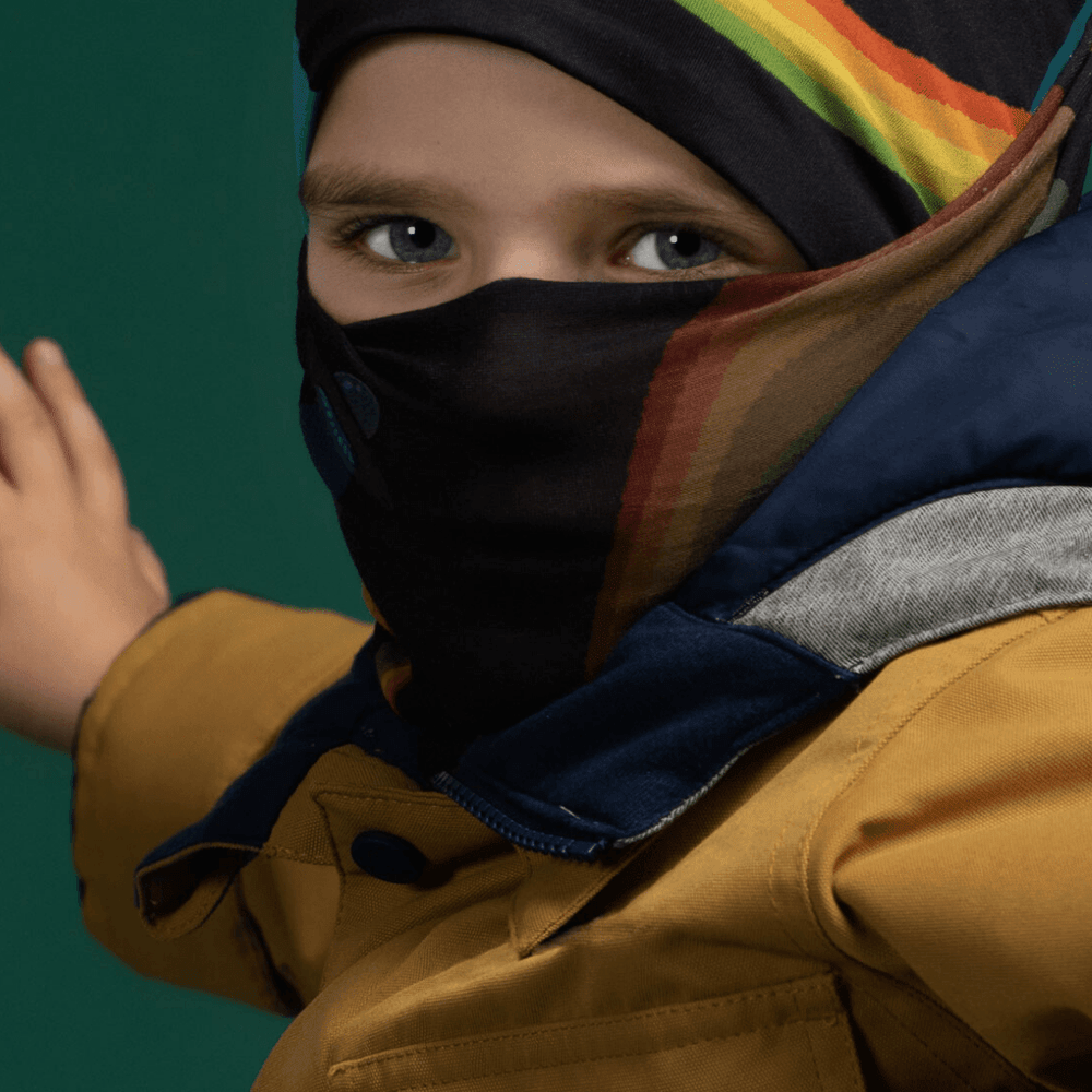 Enfant portant une veste jaune et un cache-cou comme protection visage avec un motif arc-en-ciel.