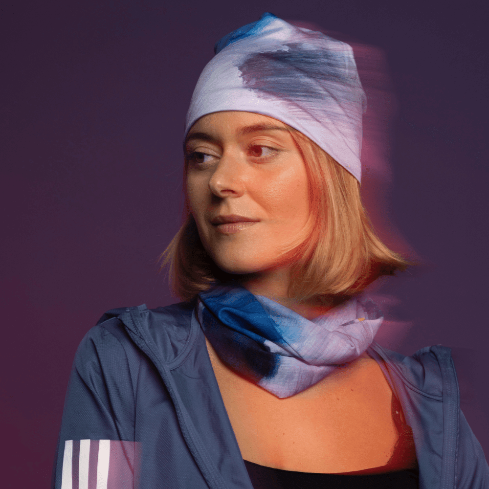 Une femme regarde sur le côté, portant une veste bleue avec un bandana noué en tuque et un autre comme cache-cou, avec une lueur rouge-orange.