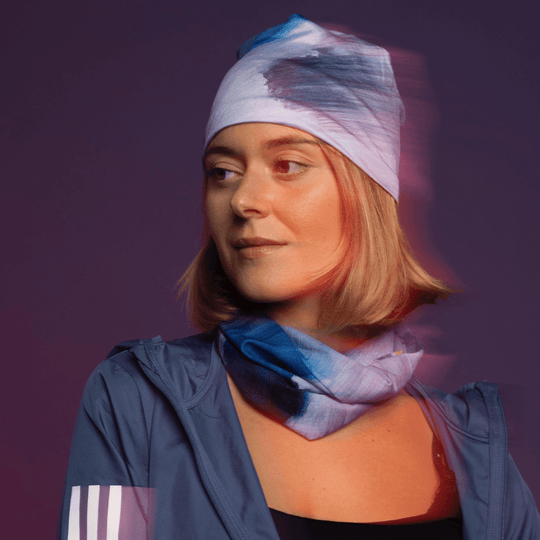 Une femme regarde sur le côté, portant une veste bleue avec un bandana noué en tuque et un autre comme cache-cou, avec une lueur rouge-orange.