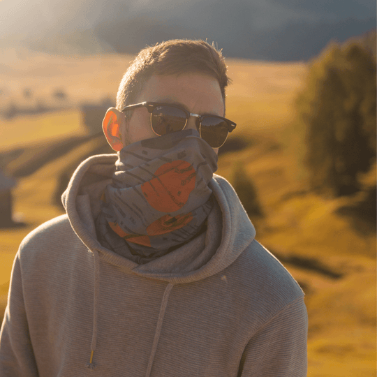 Un homme en sweat à capuche gris porte un tube multifonction comme masque facial sur un fond extérieur flou.