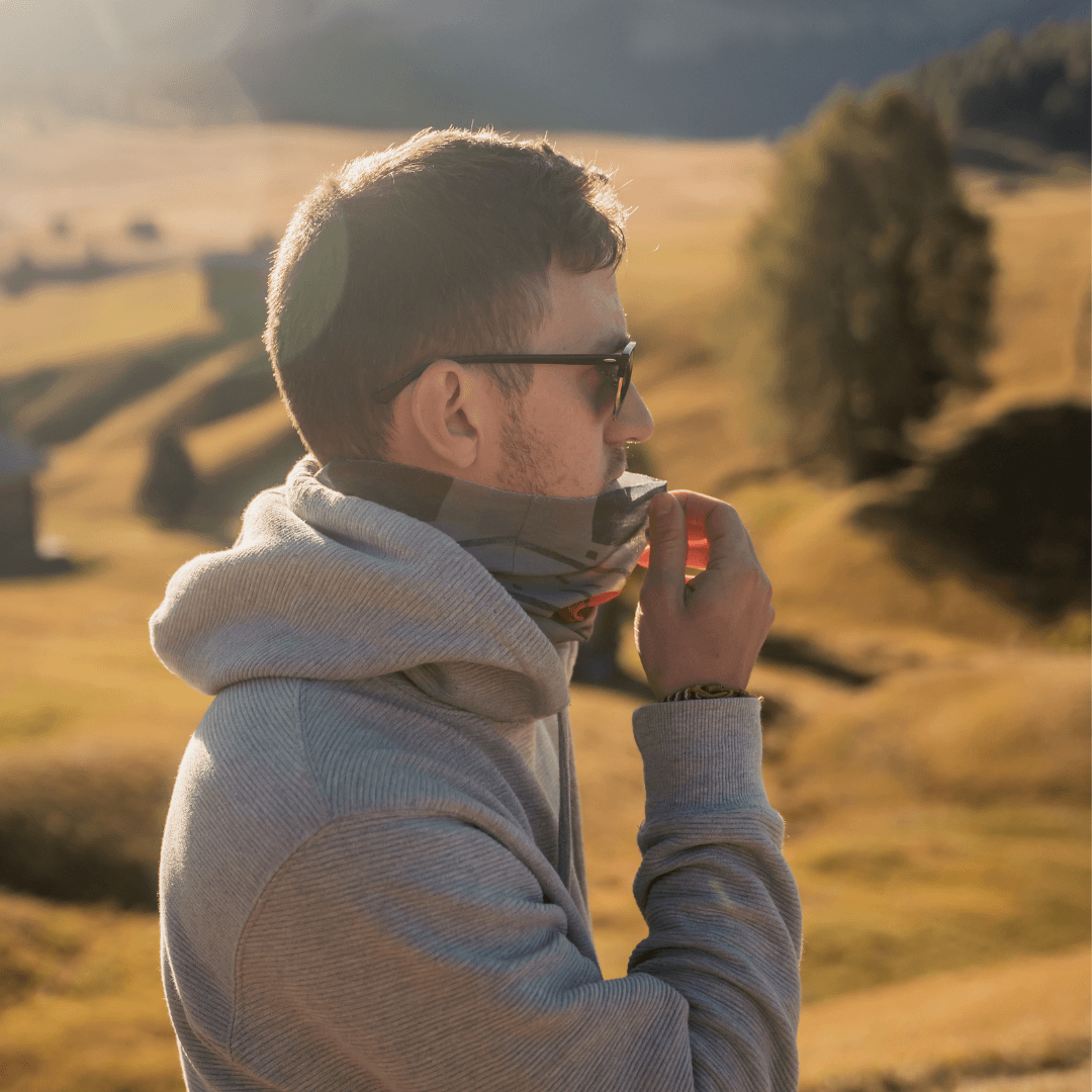 Un homme portant des lunettes de soleil et un sweat à capuche gris ajuste un cache-cou multifonction.