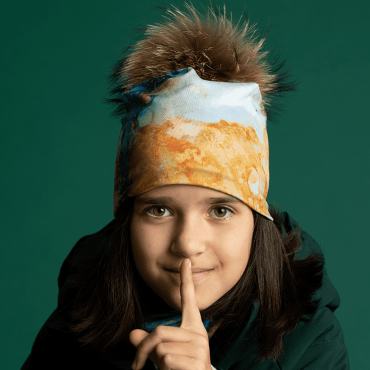 Une jeune fille portant la tuque et la tuque "Marbre Océan" sourit directement à la caméra, le doigt sur ses lèvres.