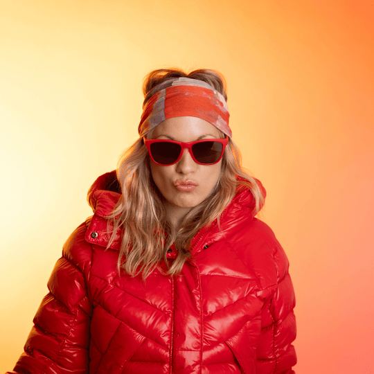 Woman in a red puffer jacket and sunglasses, posing with the Pink &amp; Flames tube as a headband.