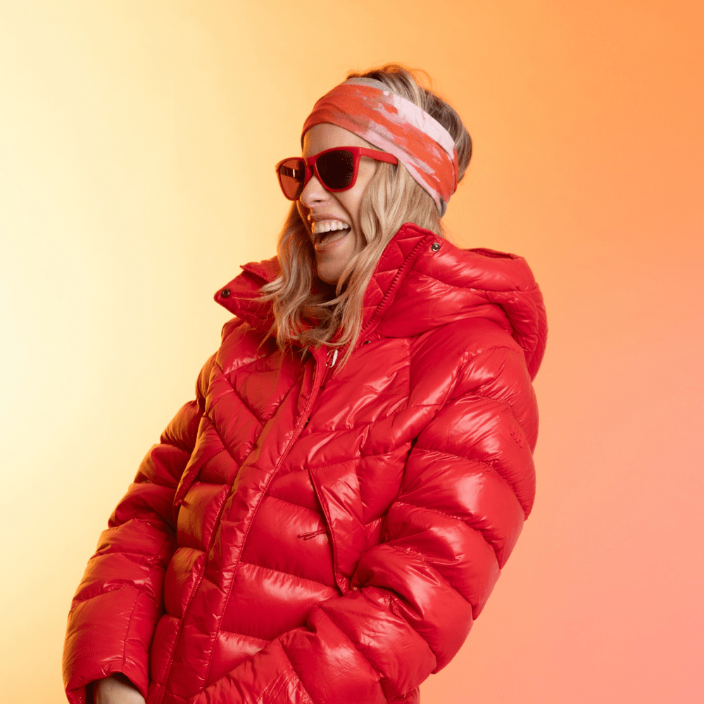 Woman wearing a red puffer jacket and sunglasses, with the Pink & Flames tube as a headband.