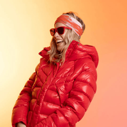 Woman wearing a red puffer jacket and sunglasses, with the Pink &amp; Flames tube as a headband.