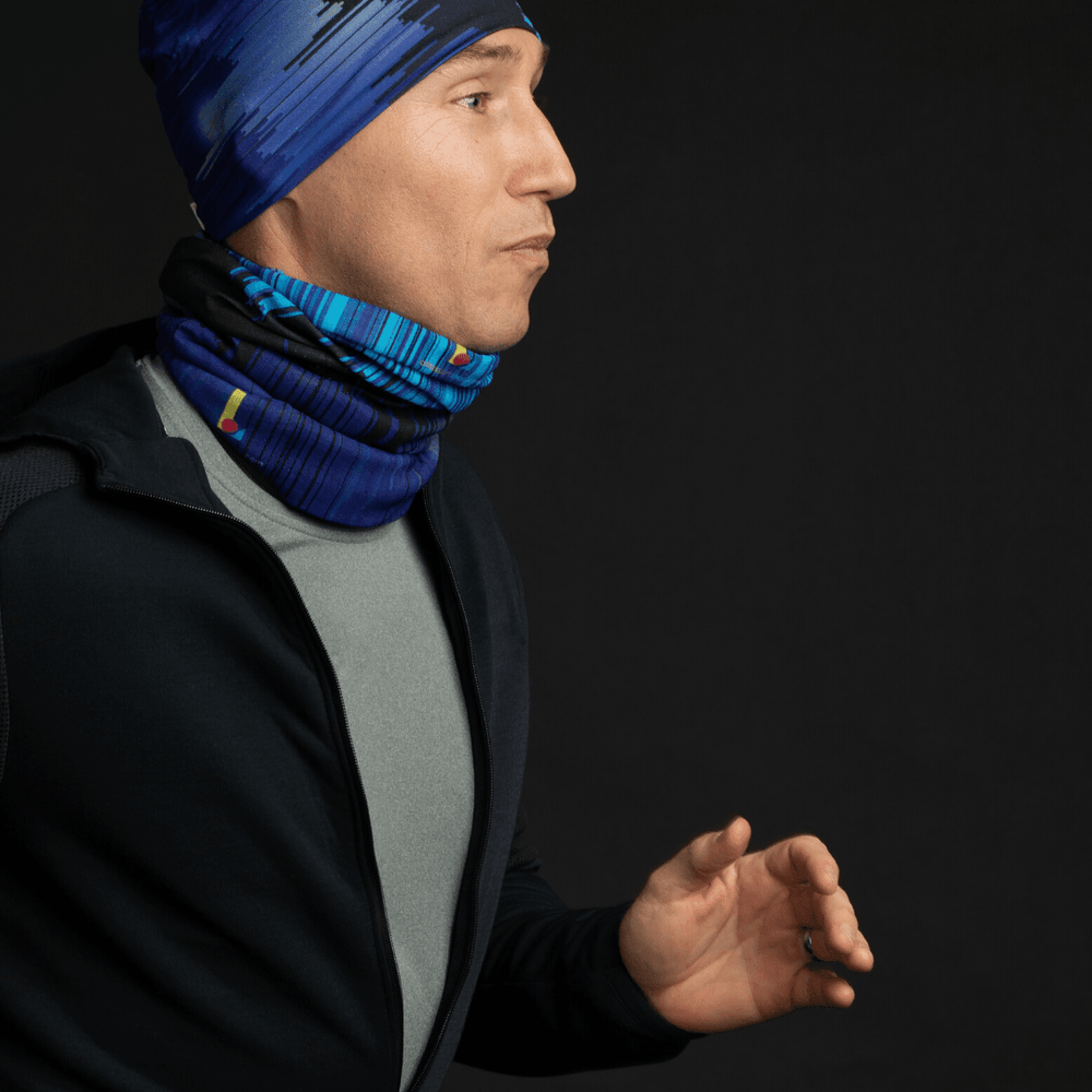 Un homme portant un t-shirt gris et un sweat à capuche foncé, avec une tuque bleu abstrait et un cache-cou assorti.