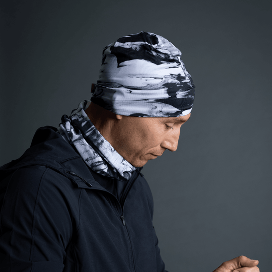 Un homme portant le tube à motif abstrait noir et blanc comme tuque et cache-cou avec une veste foncée.
