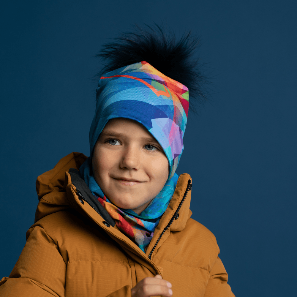 Un jeune garçon portant un manteau d'hiver jaune moutarde, une tuque assortie avec un pompon noir et un cache-cou coloré.