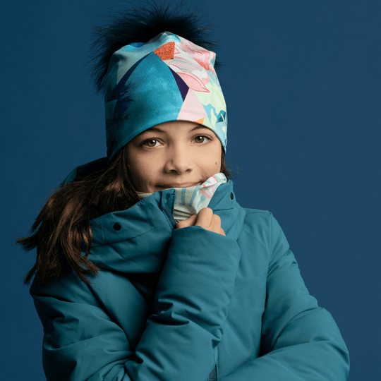 Une jeune fille portant une veste de ski turquoise, avec le cache-cou et la tuque assortis.