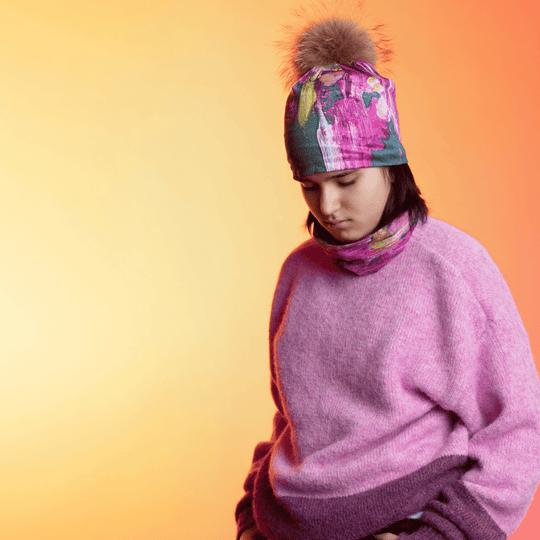 A young person wearing a pink sweater and a beanie and neck warmer with abstract floral art.