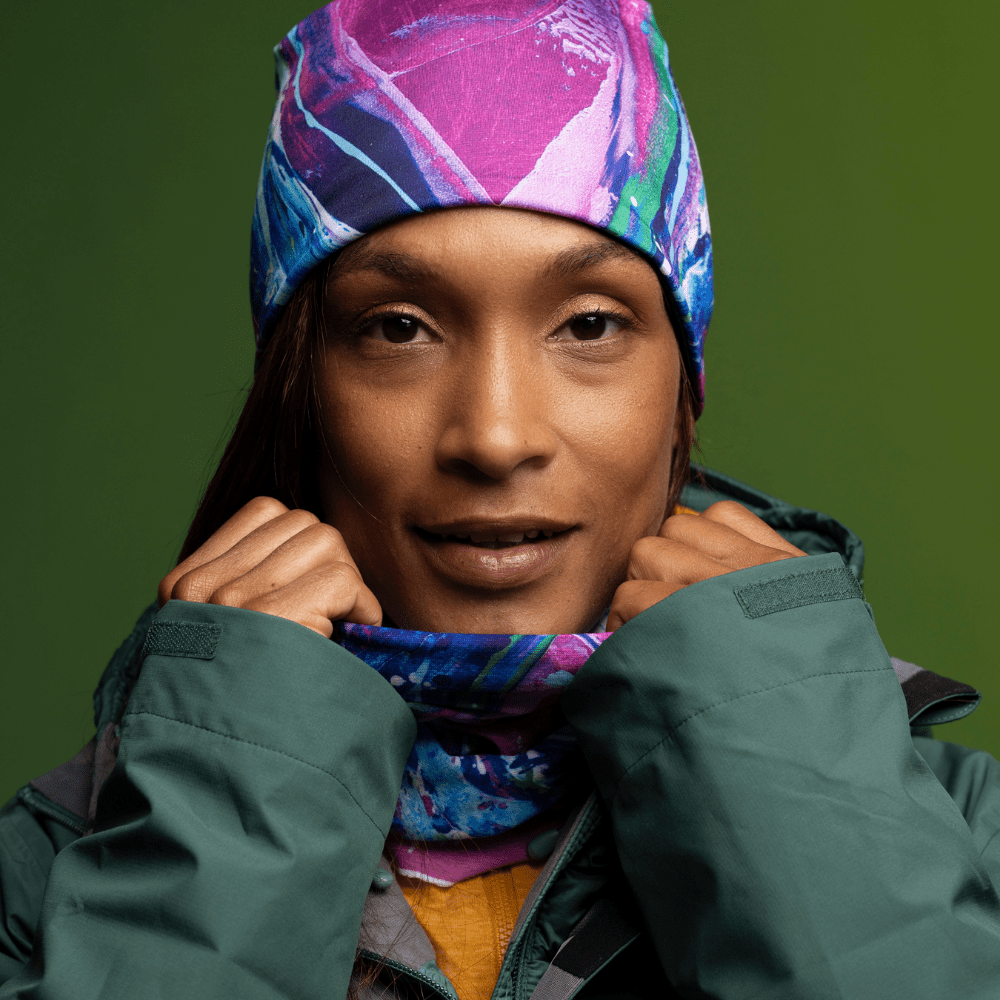 Une femme portant une veste d'hiver verte relève son col, révélant un cache-cou coloré à imprimé artistique assorti à la tuque qu'elle porte.