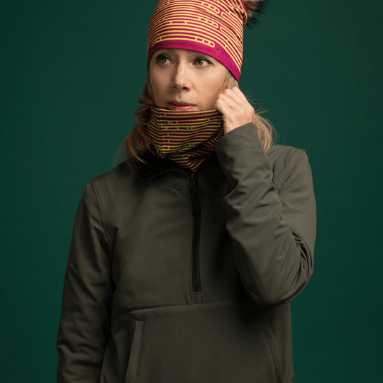 Woman wearing a green jacket and a patterned neck tube, touching the fabric near her neck.
