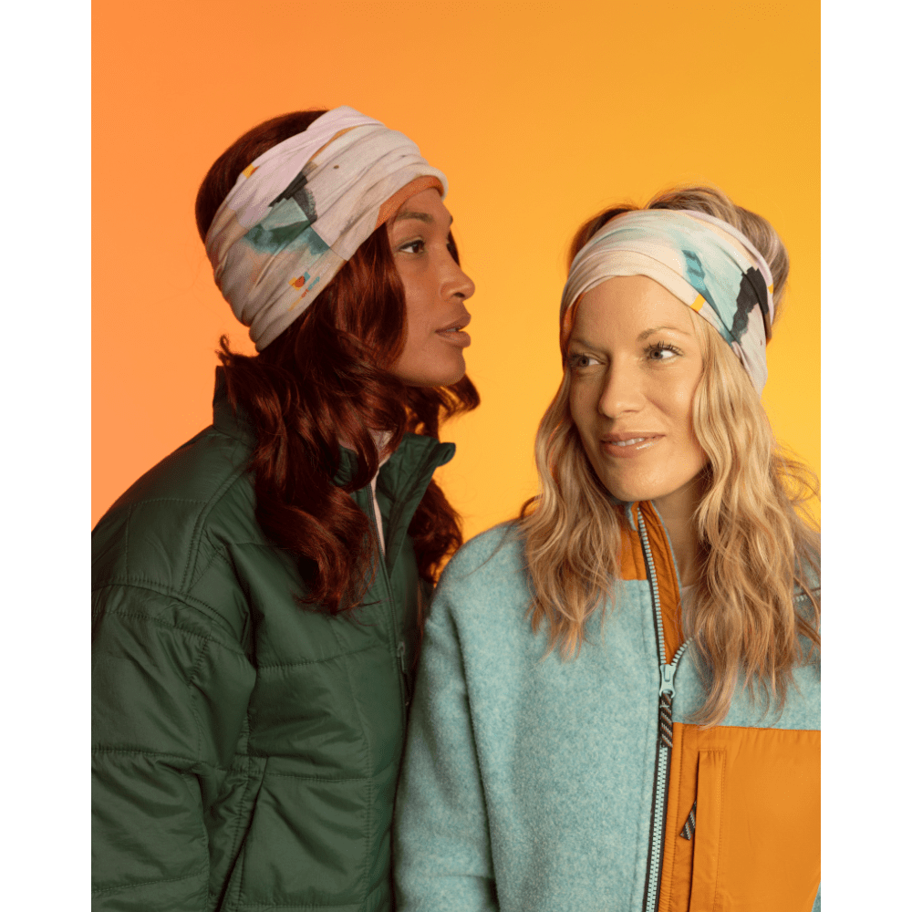 Deux femmes portant le tube multifonction POLAR Accent Marine comme bandeau sur un fond dégradé orange et jaune vif.