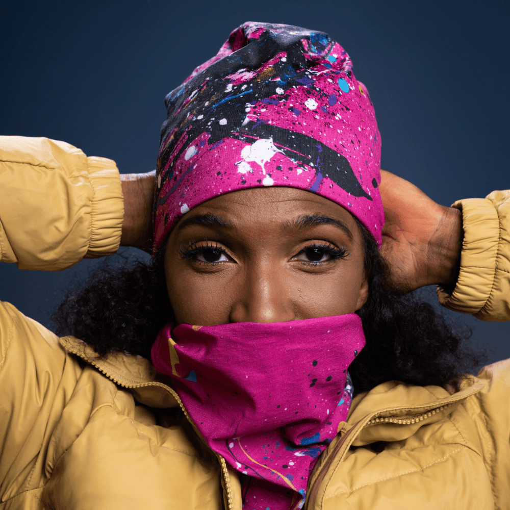 Une femme portant une veste d'hiver jaune remonte un tube à motif abstrait de peinture rose, bleue et noire sur son visage.