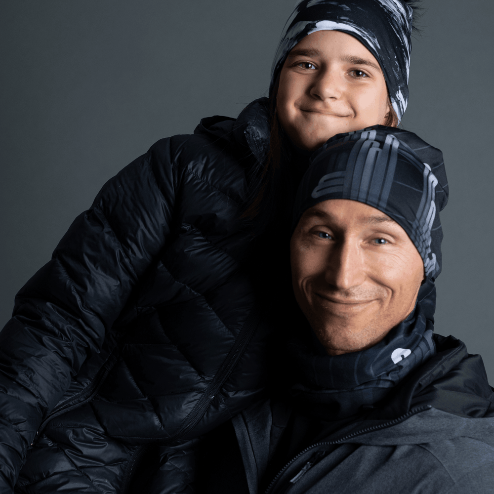 Un homme et un enfant portant des tuques et des cache-cous noirs assortis avec un motif graphique gris, emmitouflés dans des manteaux d'hiver.