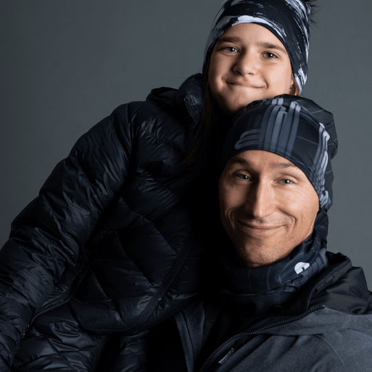 Un homme et un enfant portant des tuques et des cache-cous noirs assortis avec un motif graphique gris, emmitouflés dans des manteaux d&