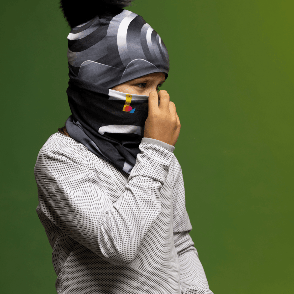 Child wearing a grey waffle-knit shirt and a black and grey abstract print neck tube pulled up as a face covering.