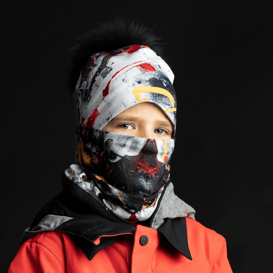 Close-up of a child wearing the Red and Black Removable Pompom Beanie and neck gaiter as a face mask, in front of a black background.
