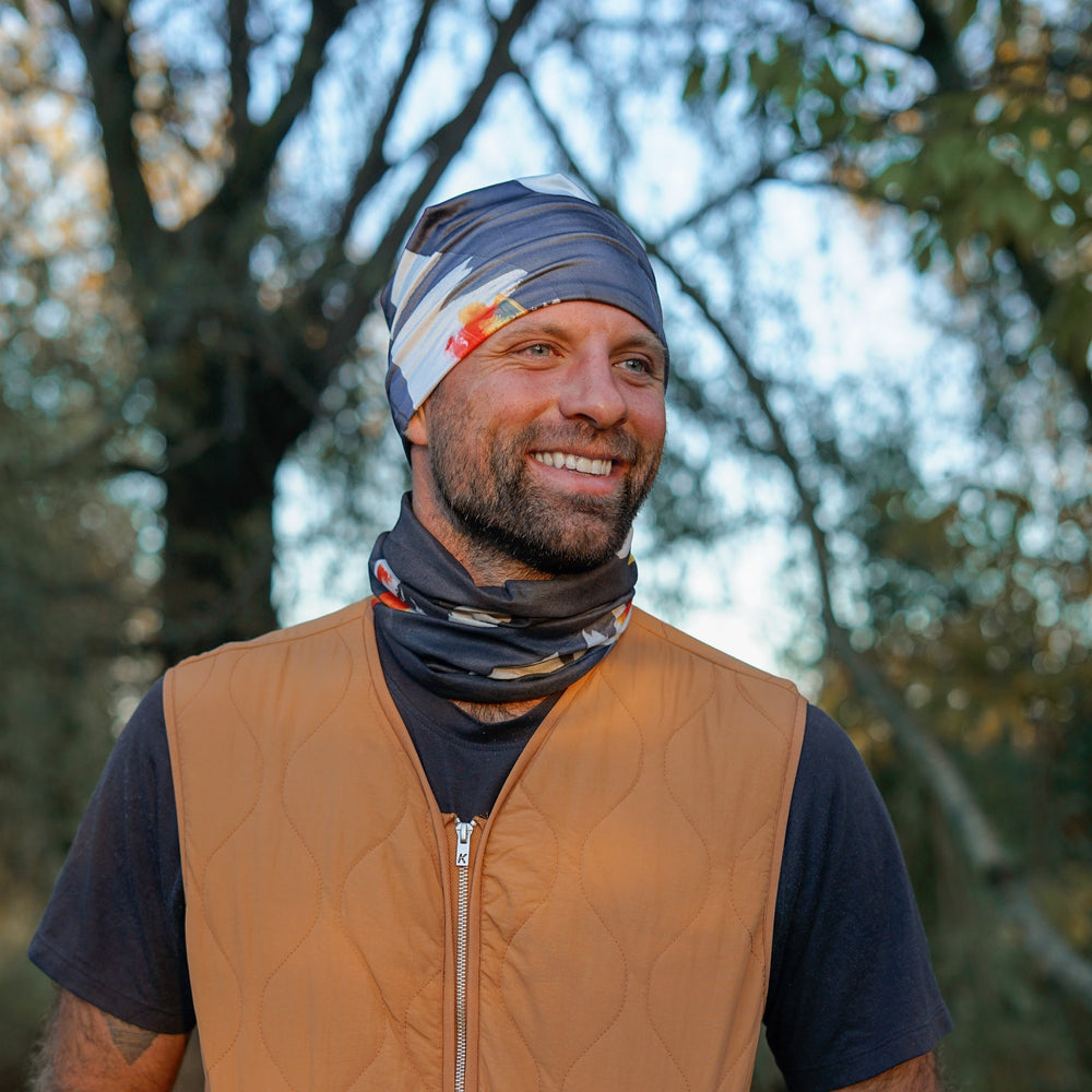 Homme portant un tube bandana en bandeaux et cache-cou, souriant à l'extérieur.