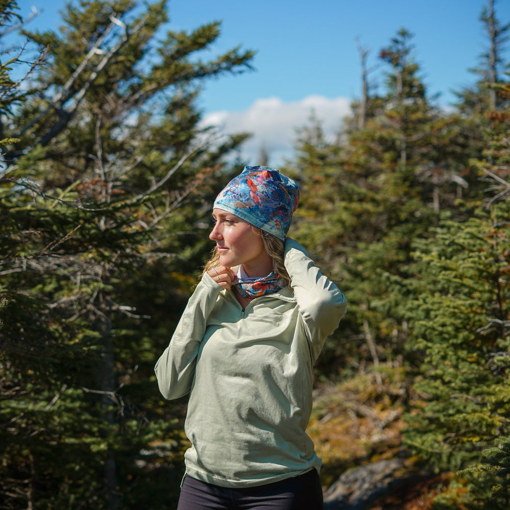 Woman wearing the Sphénédon Beanie and matching neck gaiter while hiking in a forest.