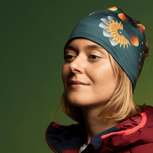 Femme portant une tuque vert foncé à imprimé floral, souriant sur fond vert.