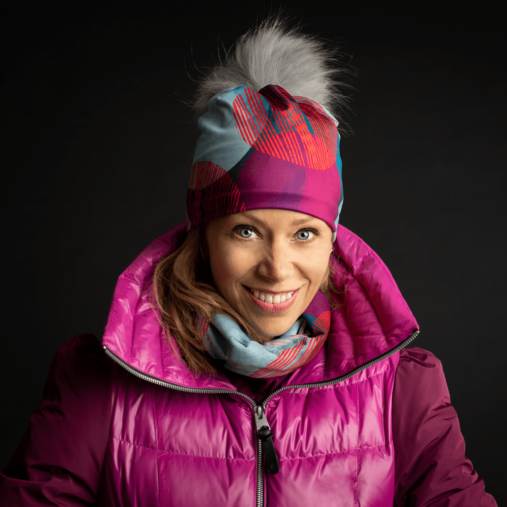 Femme portant la tuque Pois-Bleu avec pompon gris détachable, un cache-cou assorti et une veste rose.