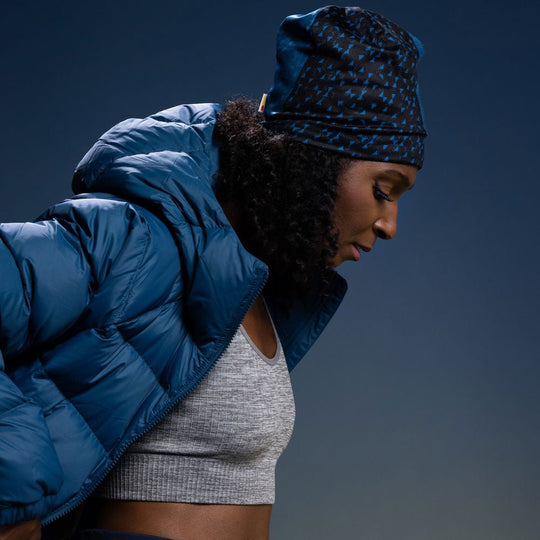 Une femme portant la tuque Flakes Bleu Canard avec une veste matelassée bleu canard et un soutien-gorge de sport gris.
