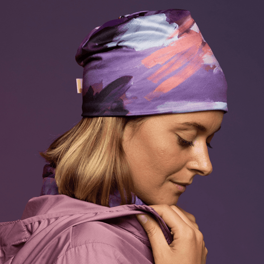 Femme portant une tuque à motif abstrait violet et un cache-cou assorti, avec une veste rose.