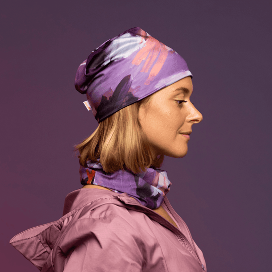 Une femme de profil porte une tuque et un tube assortis avec un imprimé floral, superposés sur une veste rose.