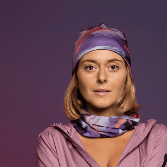 Une femme porte une tuque et un tube assortis avec un imprimé floral, posant sur fond violet.