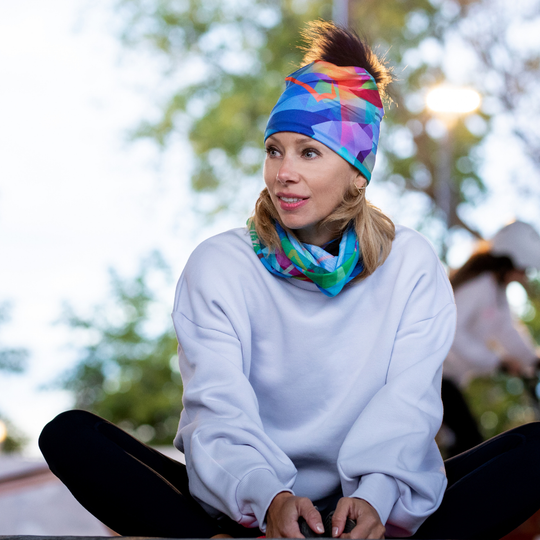 Une femme portant la tuque unisexe Fast Triangles avec un cache-cou assorti, assise à l&