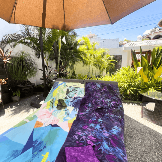 Wisteria Luxury Microfiber Towel and another art towel draped on outdoor lounge chairs under a sun umbrella.