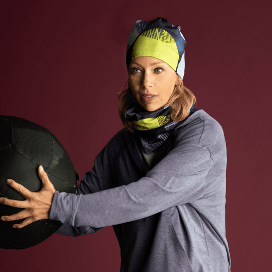 Woman wearing a matching Yellow-Dots beanie and neck tube while holding a medicine ball.