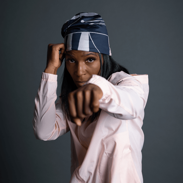 Woman boxing and wearing the sports cap called Geometrics designed by Valery Goulet. This active beanie is black and grey with a black pom-pom.