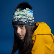 Young girl from the side, wearing a colorful sports beanie hat with black pompon. The sports cap was designed by Mégane Fortin
