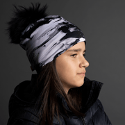 Young girl side view wearing The unisex toque B&W with abstract pattern, and a detachable black pompom. Perfect marriage between an original and trendy look with the tech features of sports toque! Ideal gift for the whole family