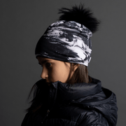 Young girl from behind, her face is turned to the side. She’s wearing The unisex toque B&W with abstract pattern, and a detachable black pompom. Perfect marriage between an original and trendy look with the tech features of sports toque! Perfect for campoing and outdoors activities. Ideal gift for the whole family