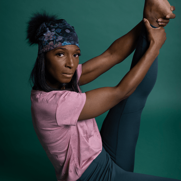 Woman doing streching with beautiful beanie hat with flowers design and black Pompon. The yoga bamboo beanie is design by Claire Anghinolphi