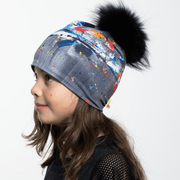 Side view of girl wearing gray, blue and white abstract pattern toque with black pompom.