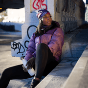 Woman sitting on stairs in the street and looking away. She is wearing the magenta Umbrella sports cap with removable pom-pom illustrated by Valery Goulet. This Lalita's Art Shop bamboo toque is designed for sports and outdoor activities. Ideal gift for women and girls, this toque can be worn in any season.