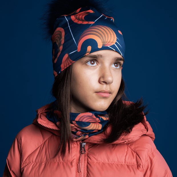  Young girl side view, wearing the Sound Barrier hat with a navy pom-pom. This sport hat was designed by the multidisciplinary artist Zaire. The bamboo beanie is perfect for toque for skiing, biking, trail riding, walking, running and snowboarding
