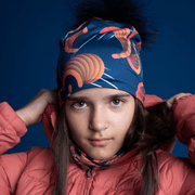 Young girl in front, putting on her hood, wearing the Sound Barrier maid designed by Zaire with a navy blue pom-pom. The bamboo beanie is perfect for outdoor activities. Best snowboarding and ski beanie.